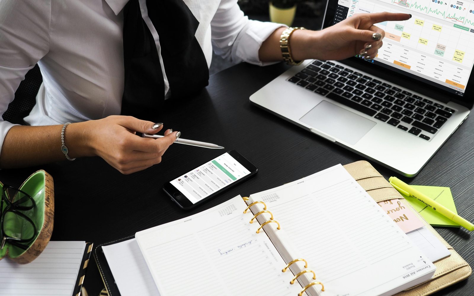 A manager working across a paper planner, a phone and a laptop